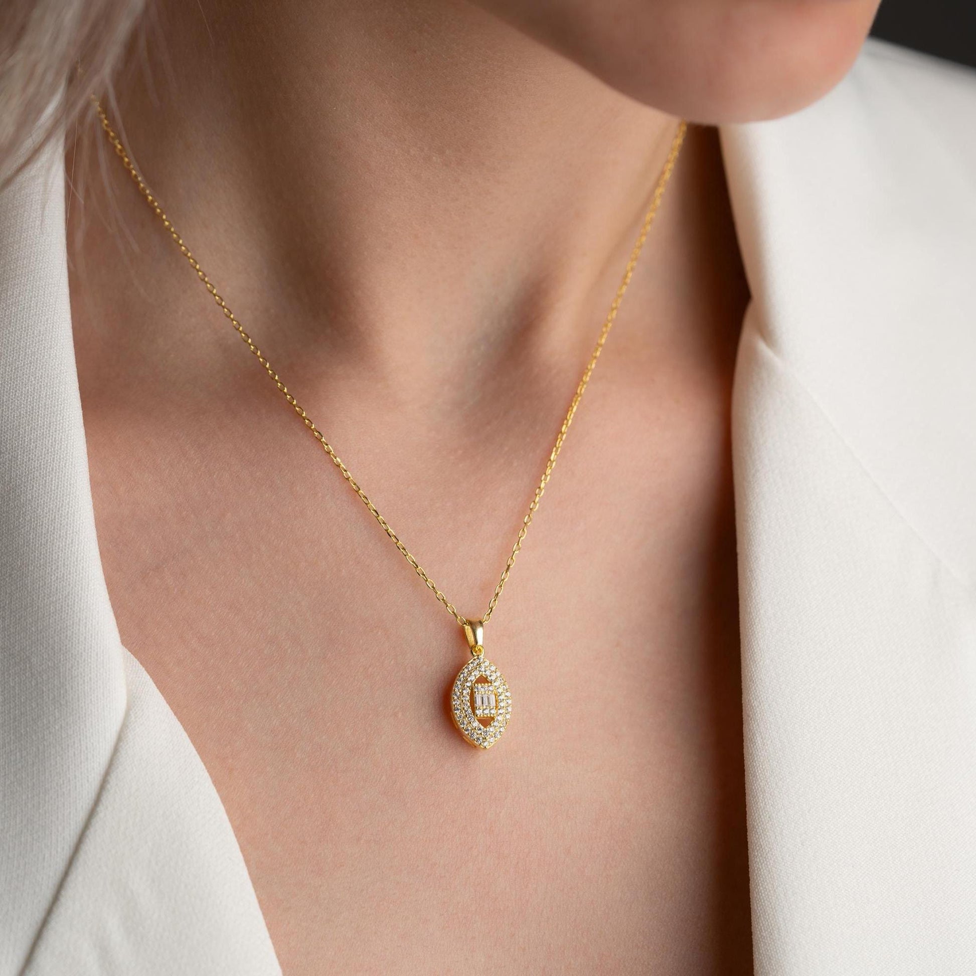 Elegant oval pendant necklace with cubic zirconia stones, available in 925 sterling silver and 14K gold plated options, displayed on a white satin background.