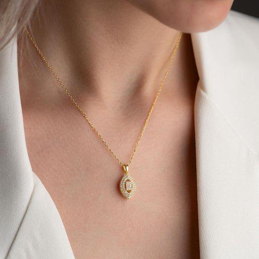 Elegant oval pendant necklace with cubic zirconia stones, available in 925 sterling silver and 14K gold plated options, displayed on a white satin background.