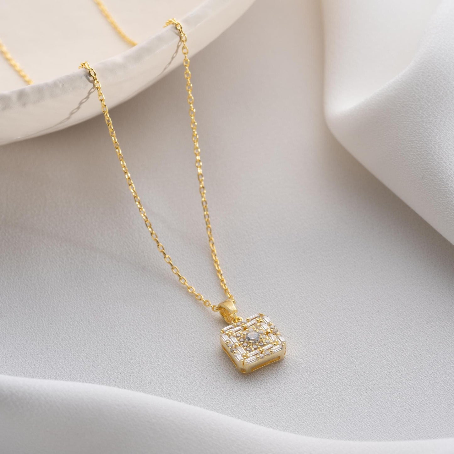 Square pendant necklace with cubic zirconia stones, available in 925 sterling silver and 14K gold plated options, displayed on a white satin background.