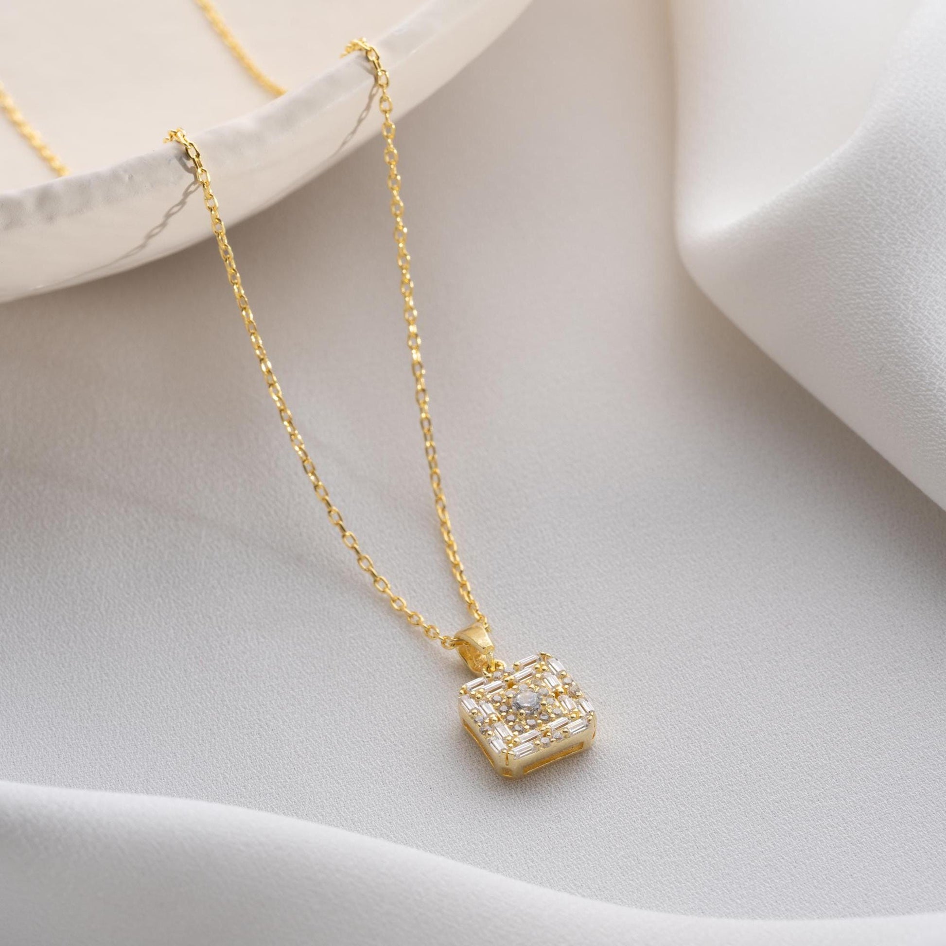 Square pendant necklace with cubic zirconia stones, available in 925 sterling silver and 14K gold plated options, displayed on a white satin background.