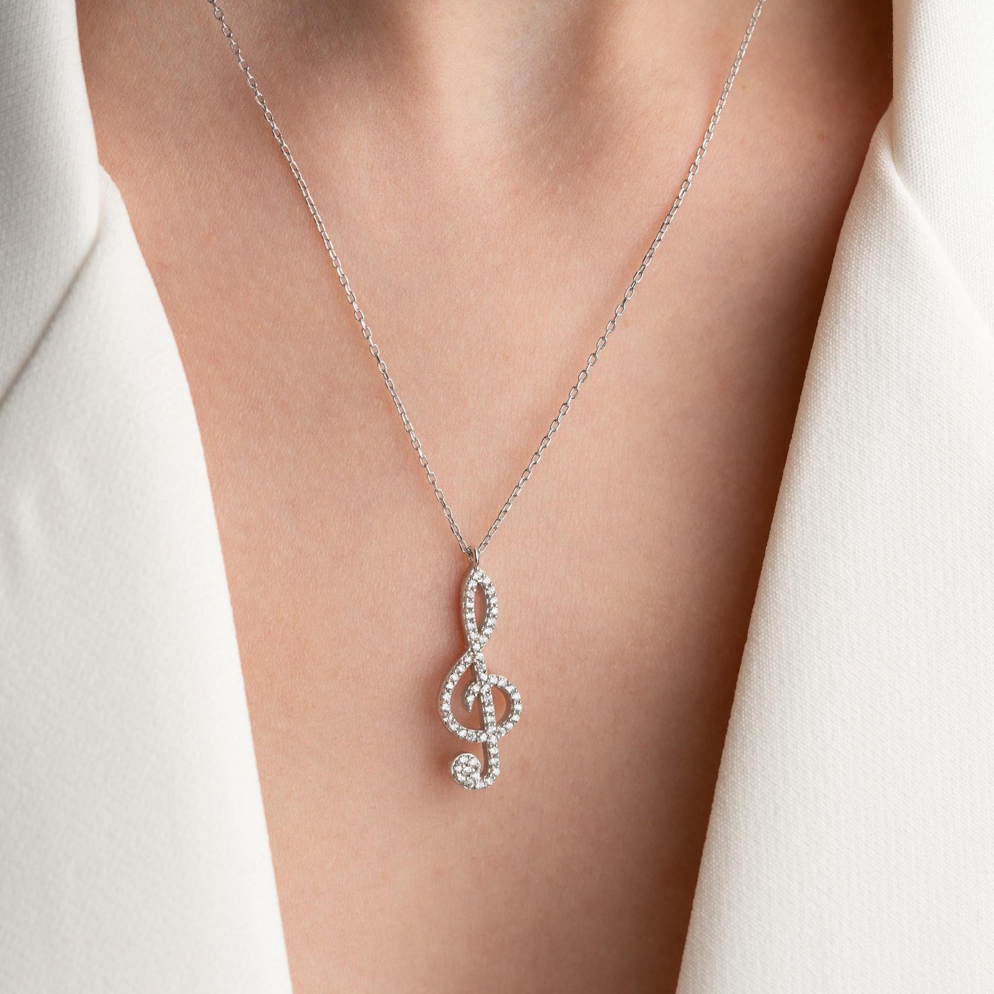 Music note necklace with cubic zirconia stones, available in 925 sterling silver and 14K gold plated options, displayed on a white satin background.