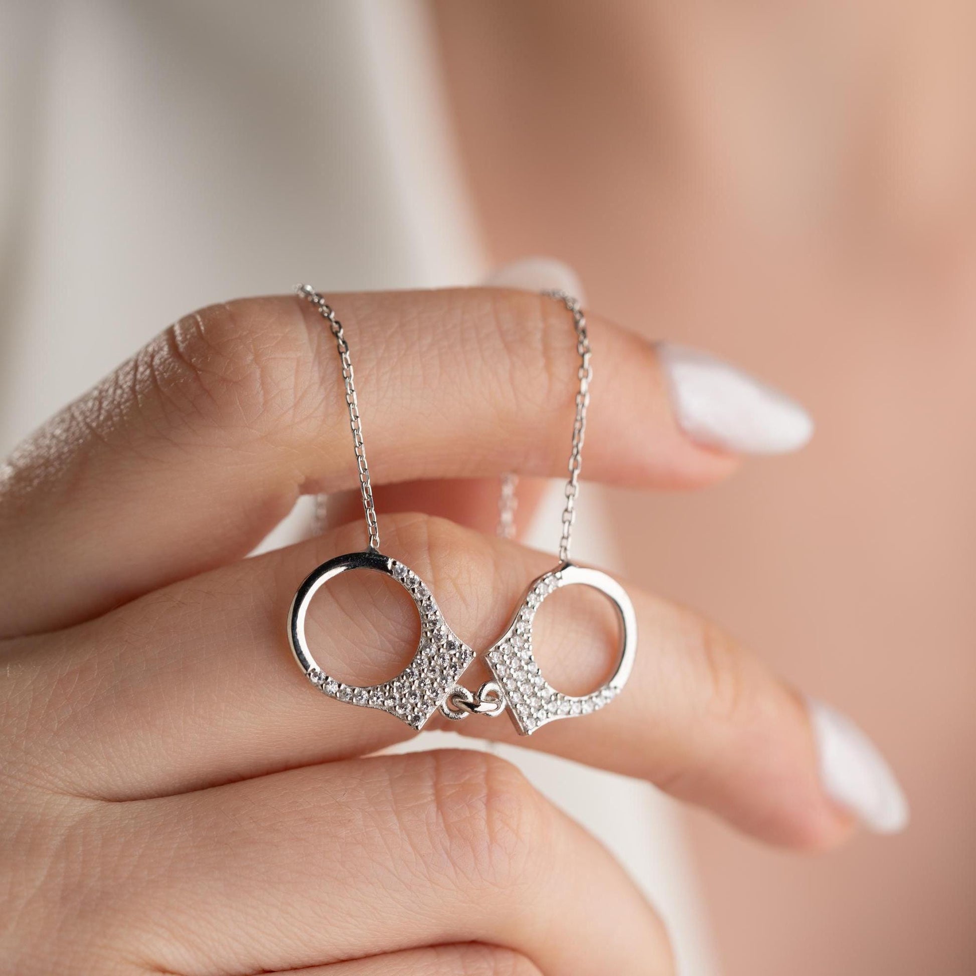 Handcuff necklace with cubic zirconia stones, available in 925 sterling silver and 14K gold plated options, displayed on a white satin background.