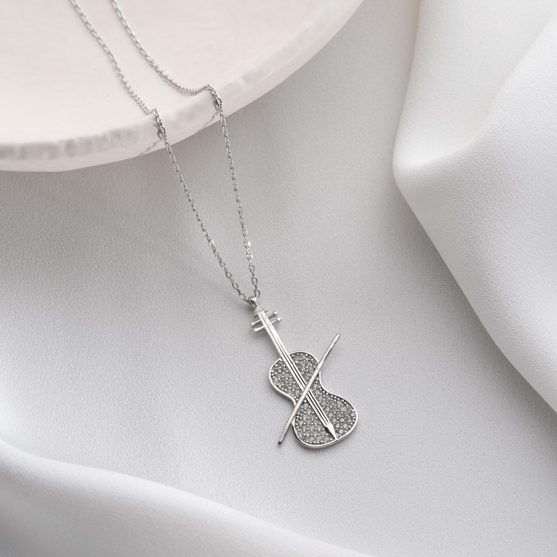 Violin-shaped necklace with cubic zirconia stones, available in 925 sterling silver and 14K gold plated options, displayed on a white satin background.