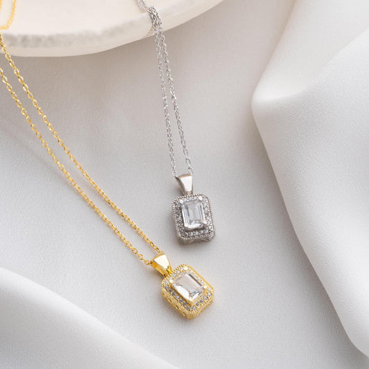 Baguette-cut pendant necklace with cubic zirconia stones, available in 925 sterling silver and 14K gold plated options, displayed on a white satin background