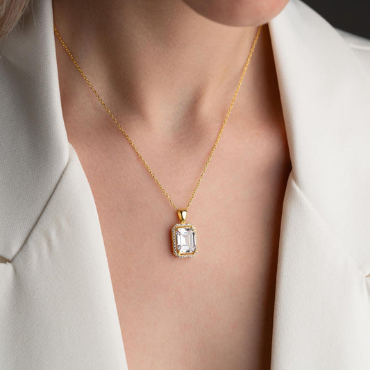 Emerald-cut pendant necklace with cubic zirconia stones, available in 925 sterling silver and 14K gold plated options, displayed on a white satin background