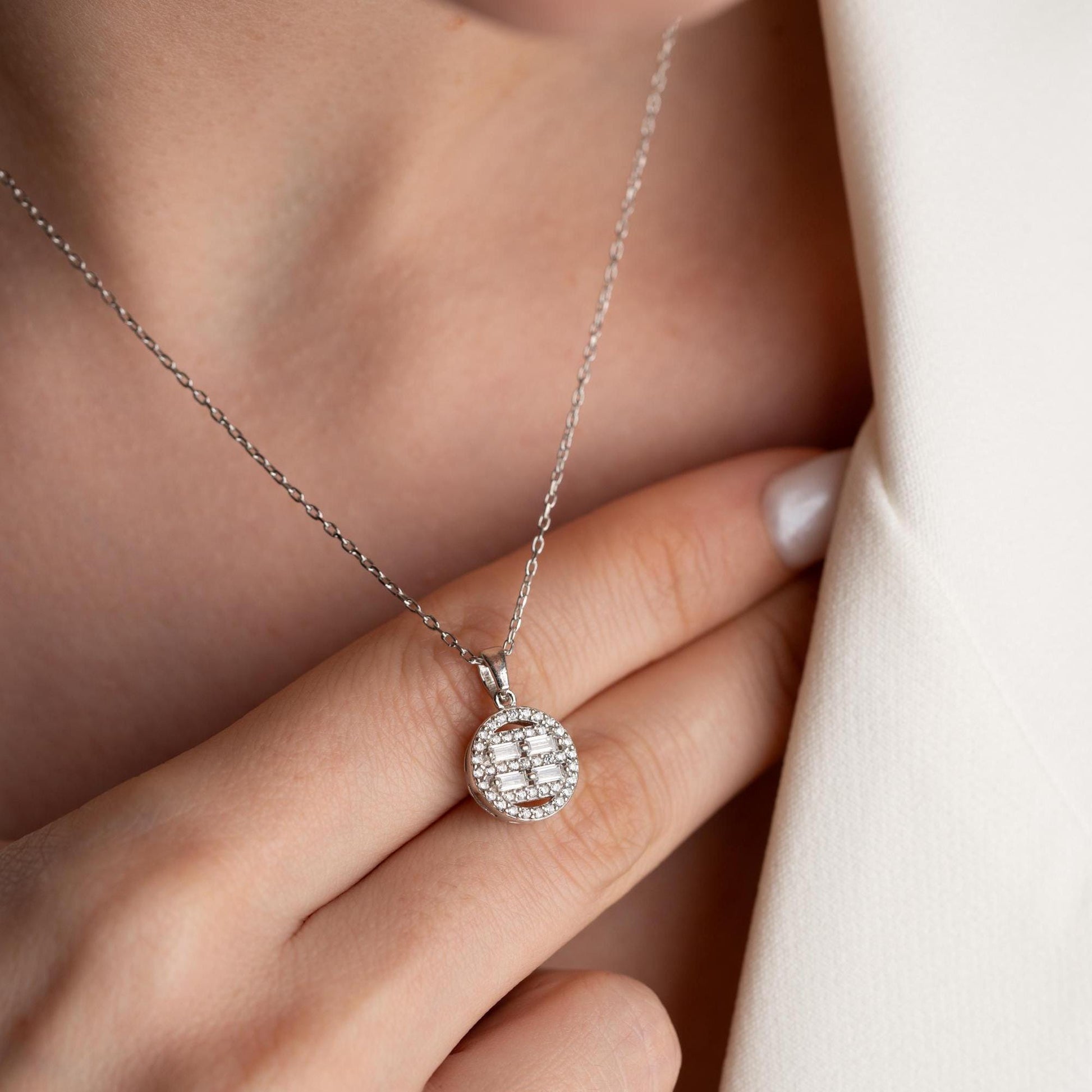 Round pendant necklace with cubic zirconia stones, available in 925 sterling silver and 14K gold plated options, displayed on a white satin background.