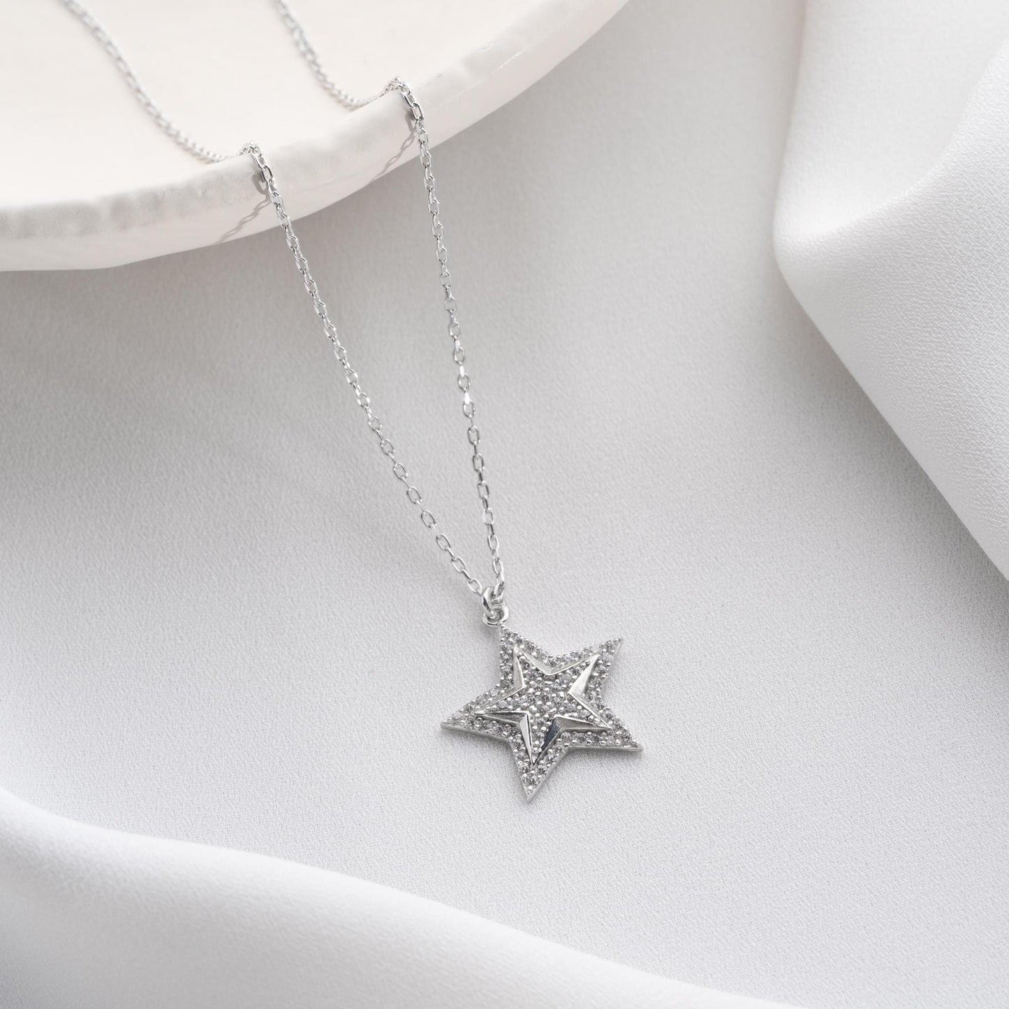 Star pendant necklace with cubic zirconia stones, available in 925 sterling silver and 14K gold plated options, displayed on a white satin background.