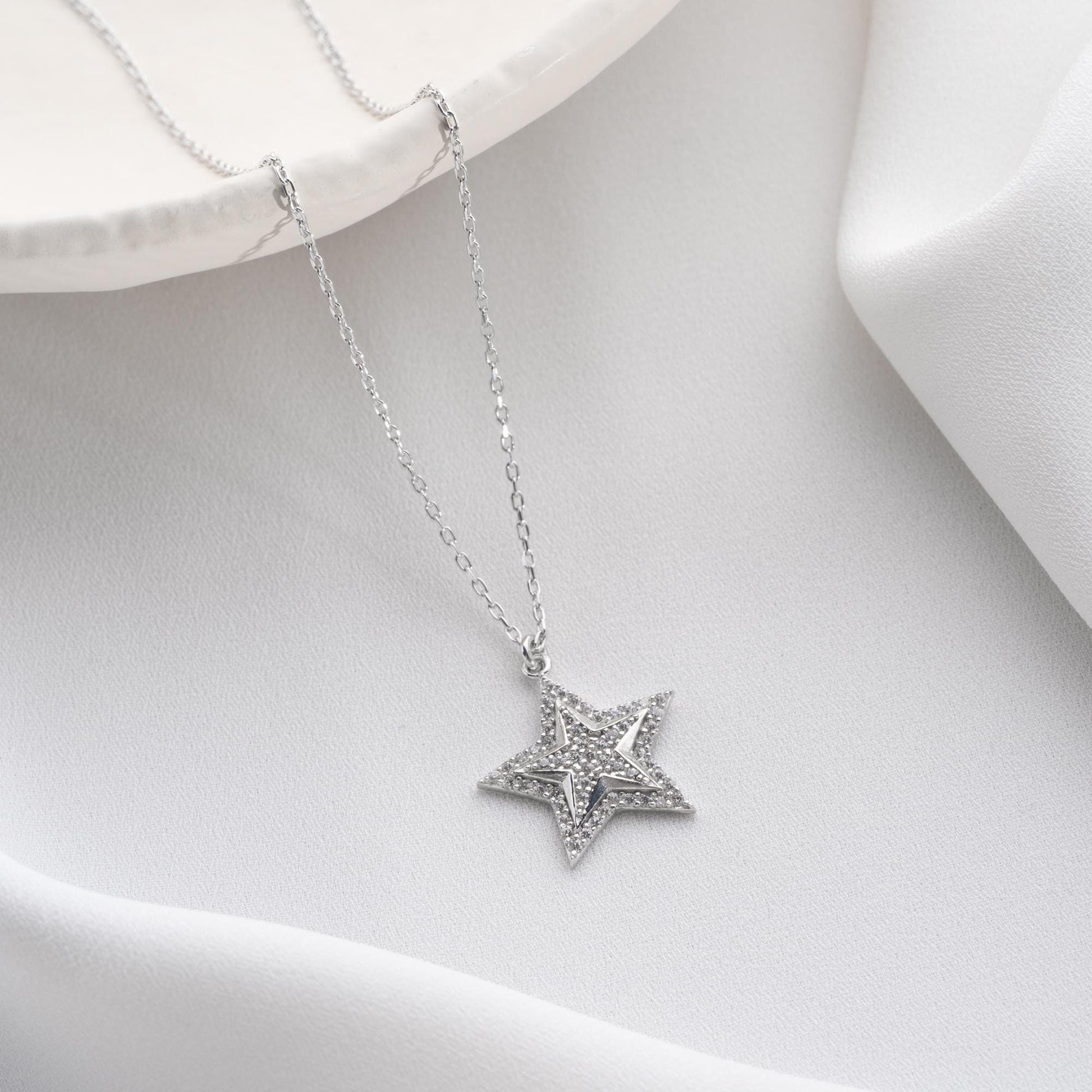 Star pendant necklace with cubic zirconia stones, available in 925 sterling silver and 14K gold plated options, displayed on a white satin background.