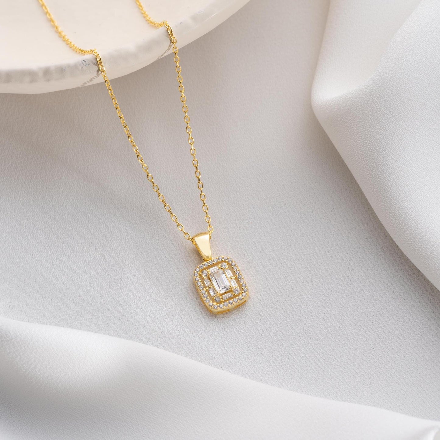 Square baguette pendant necklace with cubic zirconia stones, available in 925 sterling silver and 14K gold plated options, displayed on a white satin background.