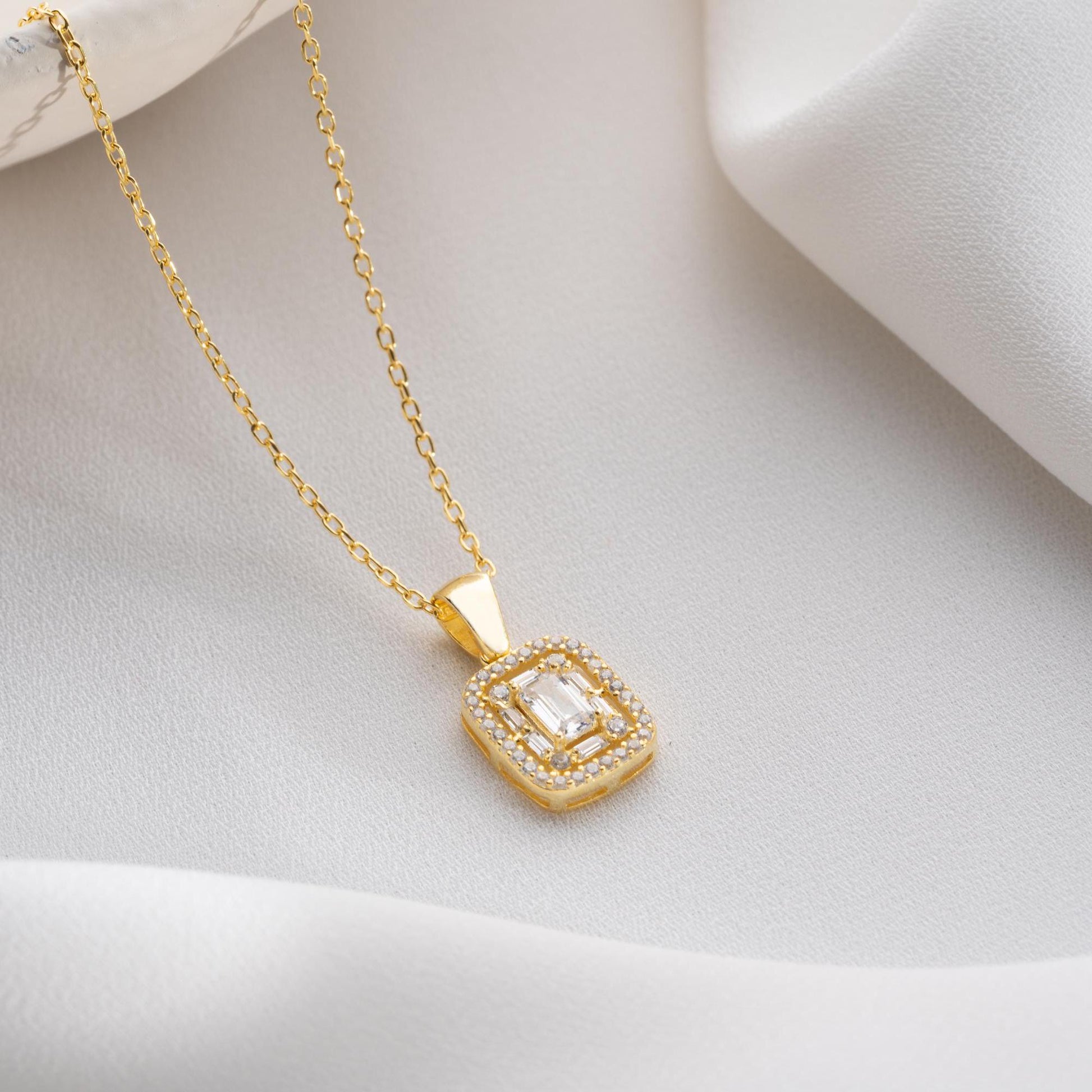 Square baguette pendant necklace with cubic zirconia stones, available in 925 sterling silver and 14K gold plated options, displayed on a white satin background.
