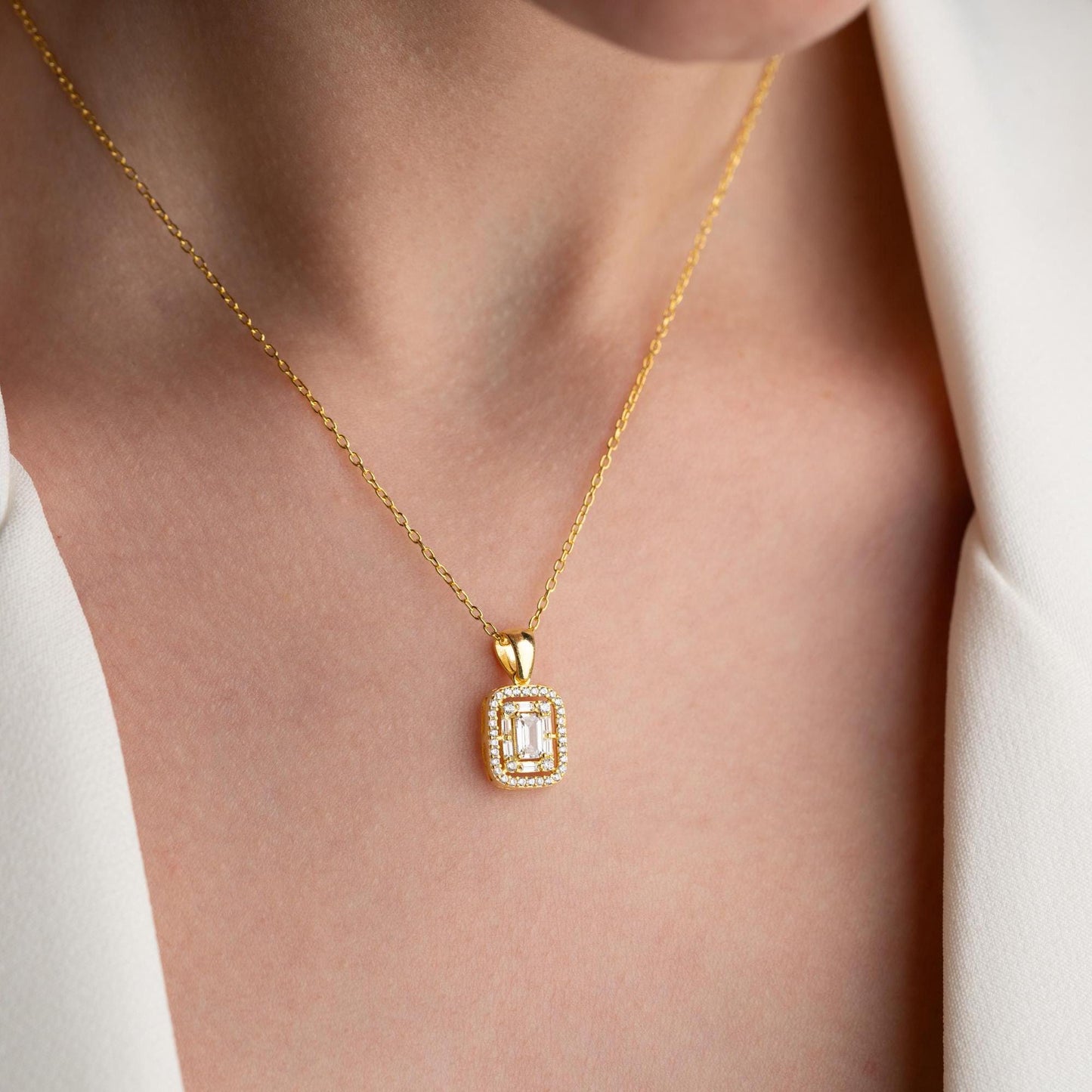 Square baguette pendant necklace with cubic zirconia stones, available in 925 sterling silver and 14K gold plated options, displayed on a white satin background.