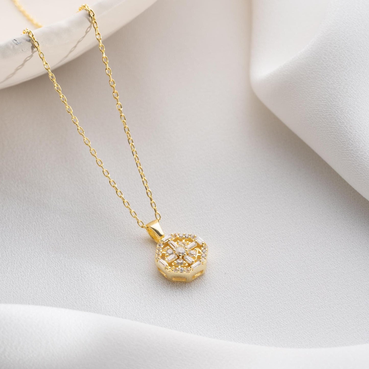 Octagon pendant necklace with cubic zirconia stones, available in 925 sterling silver and 14K gold plated options, displayed on a white satin background