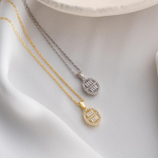 Oval pendant necklace with cubic zirconia stones, available in 925 sterling silver and 14K gold plated options, displayed on a white satin background