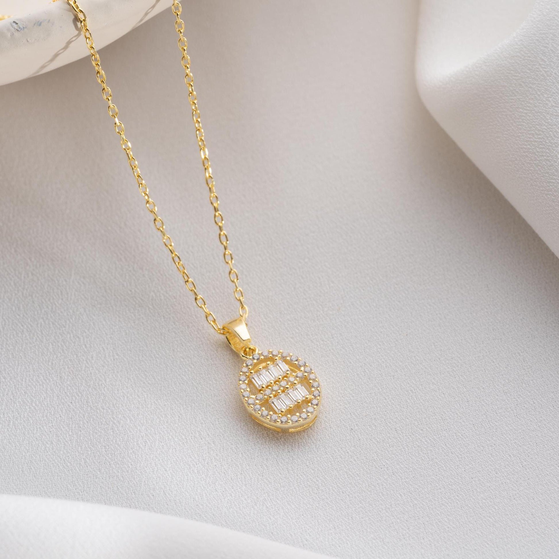 Oval pendant necklace with cubic zirconia stones, available in 925 sterling silver and 14K gold plated options, displayed on a white satin background