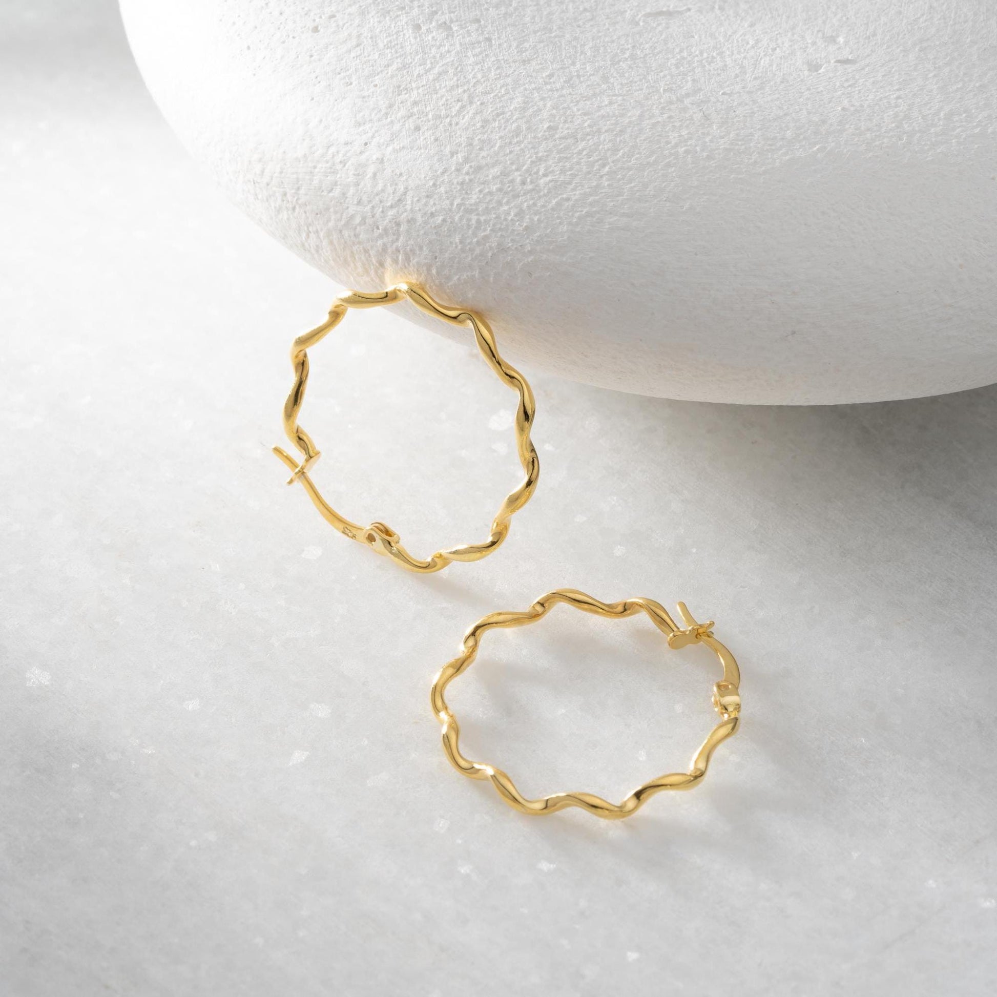 Wavy hoop earrings in 925 sterling silver and 14K gold plated options, displayed on a marble background