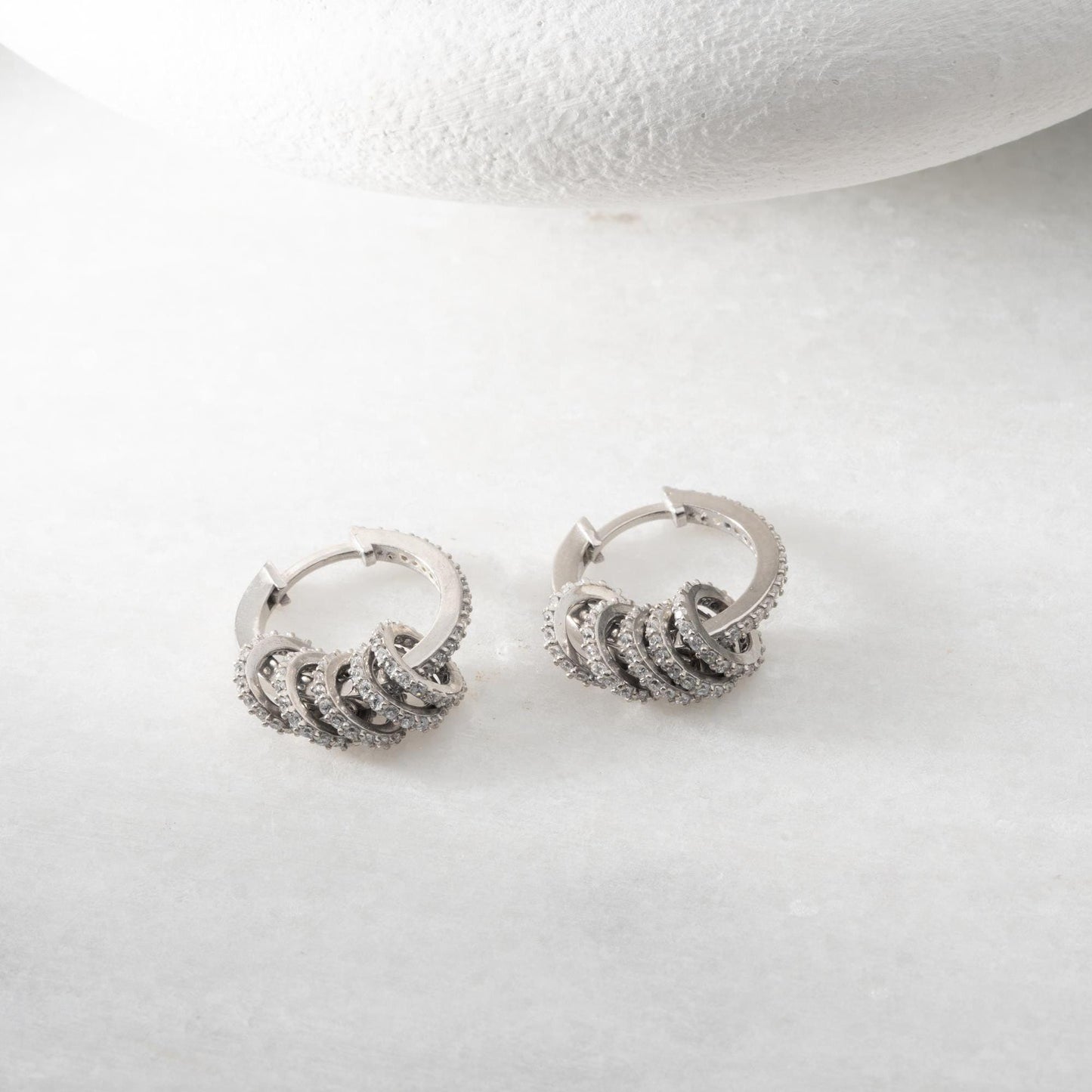 Multi-ring hoop earrings with sparkling cubic zirconia stones in 925 sterling silver and 14K gold-plated options, displayed on a marble background.