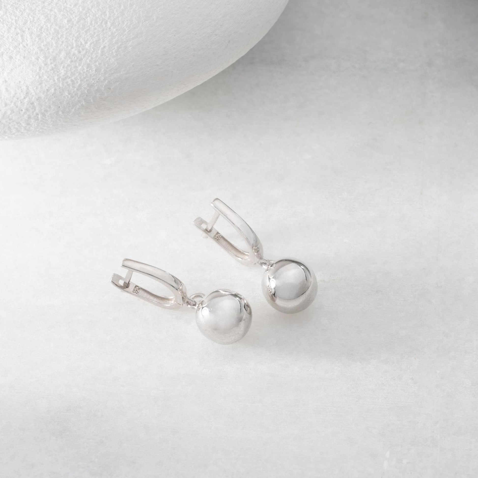 minimalist ball earrings in 925 sterling silver and 14K gold plated options, featuring a sleek design and lever-back closure displayed on a white marble background