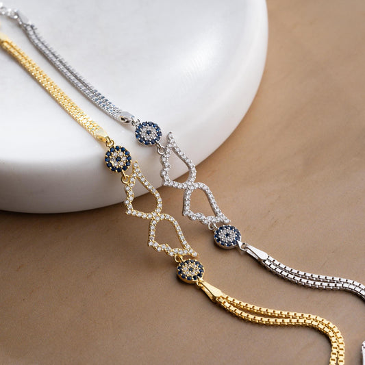 A luxurious Turkish-inspired evil eye and angel wing charm bracelet crafted in 925 sterling silver with sparkling cubic zirconia stones, available in gold and silver options.