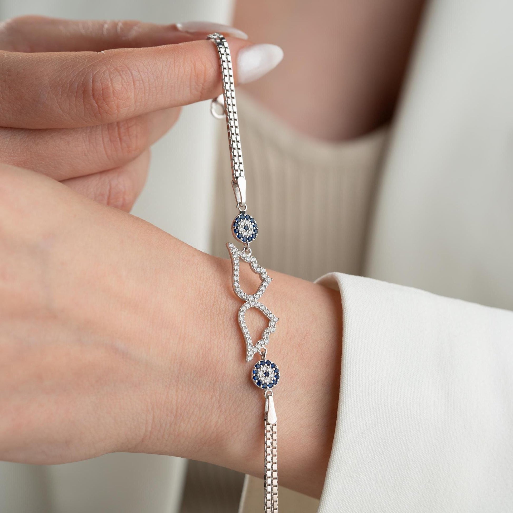 A luxurious Turkish-inspired evil eye and angel wing charm bracelet crafted in 925 sterling silver with sparkling cubic zirconia stones, available in gold and silver options.