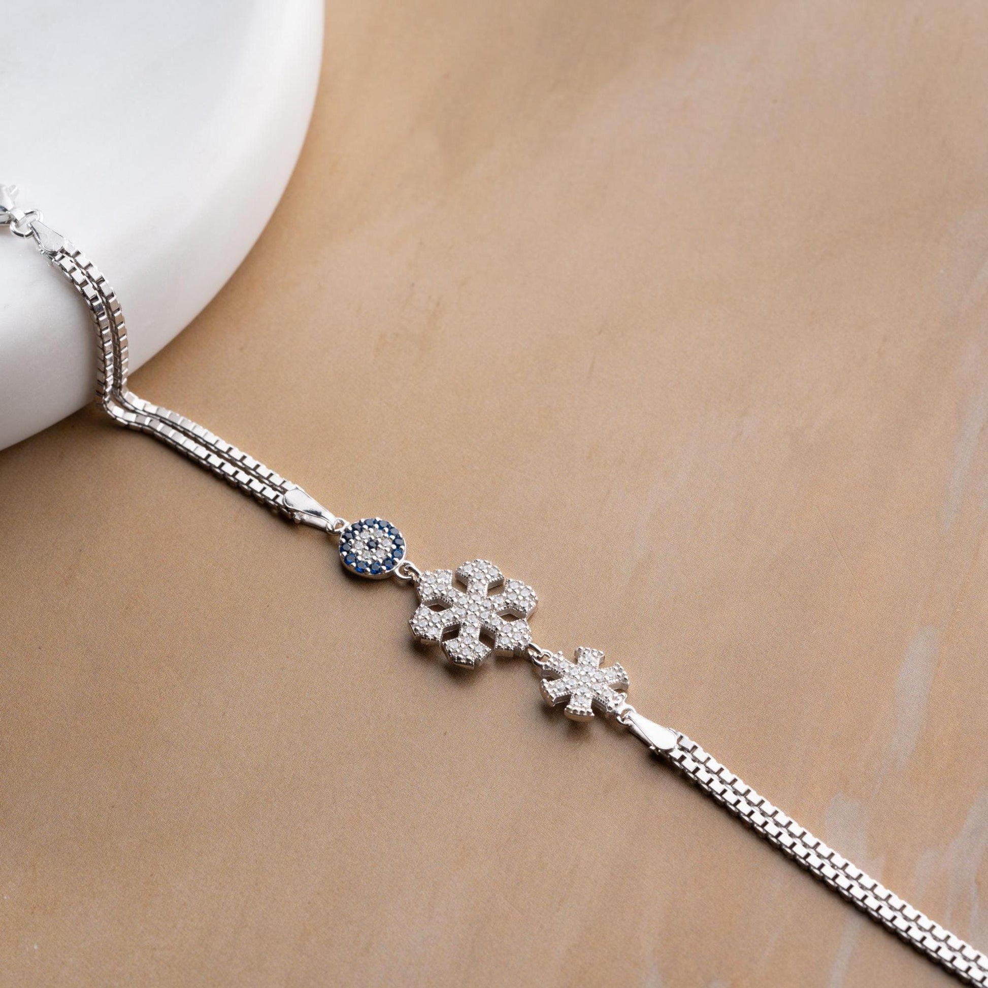 A stunning charm bracelet featuring delicate snowflake motifs and evil eye accents, crafted from 925 Sterling Silver and cubic zirconia stones, available in silver and gold finishes, ideal for festive gifting.