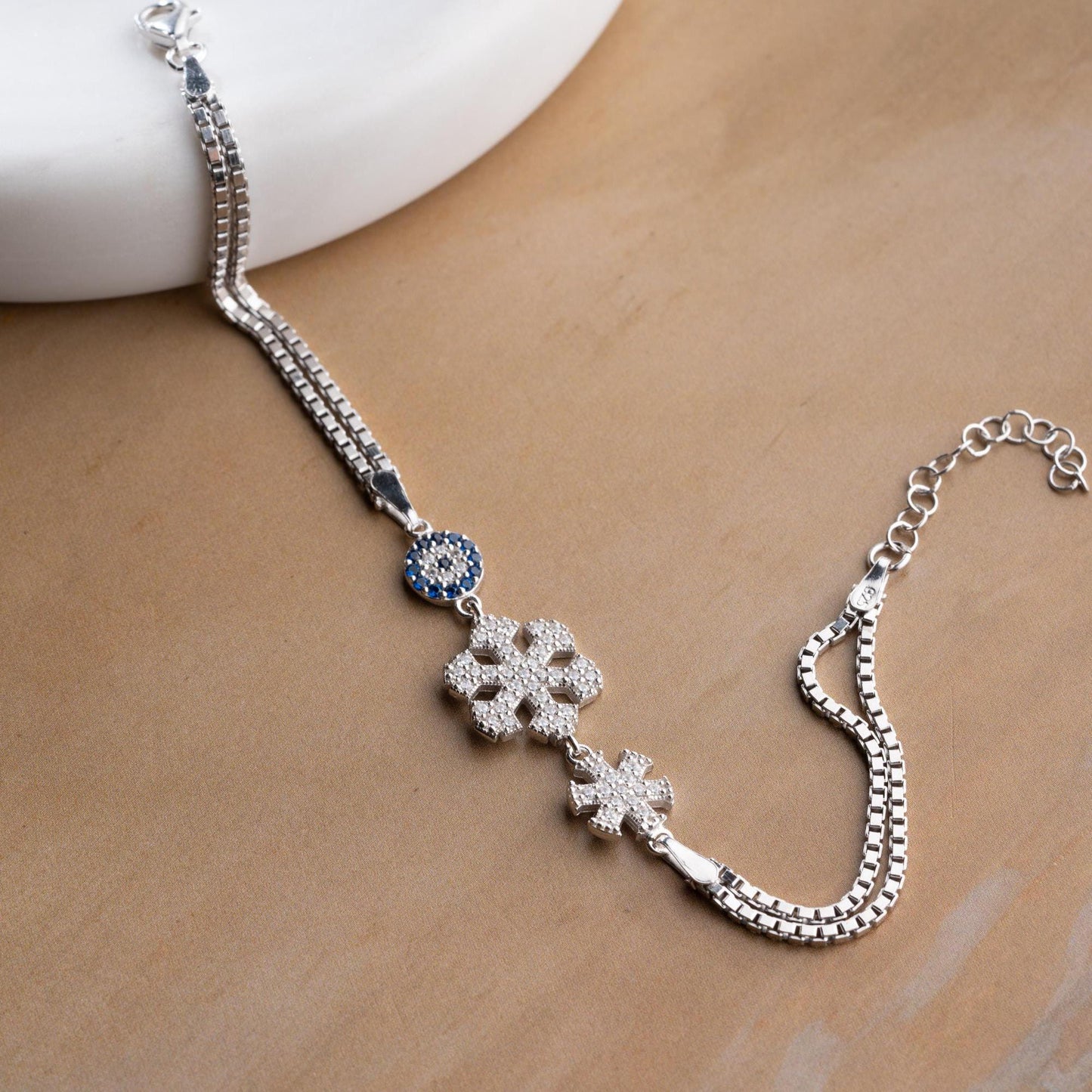A stunning charm bracelet featuring delicate snowflake motifs and evil eye accents, crafted from 925 Sterling Silver and cubic zirconia stones, available in silver and gold finishes, ideal for festive gifting.