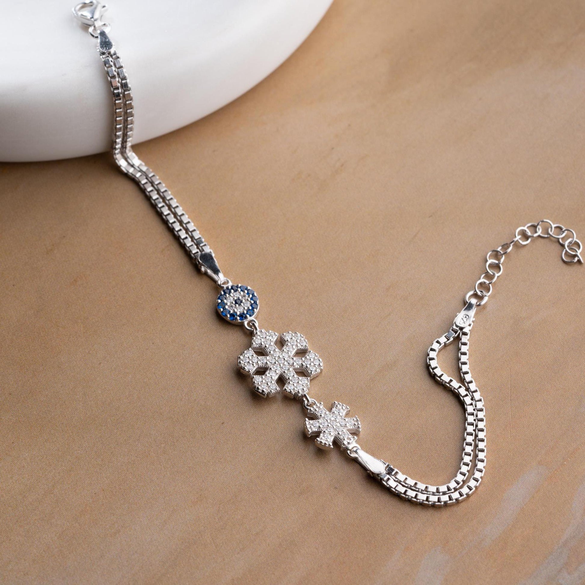 A stunning charm bracelet featuring delicate snowflake motifs and evil eye accents, crafted from 925 Sterling Silver and cubic zirconia stones, available in silver and gold finishes, ideal for festive gifting.
