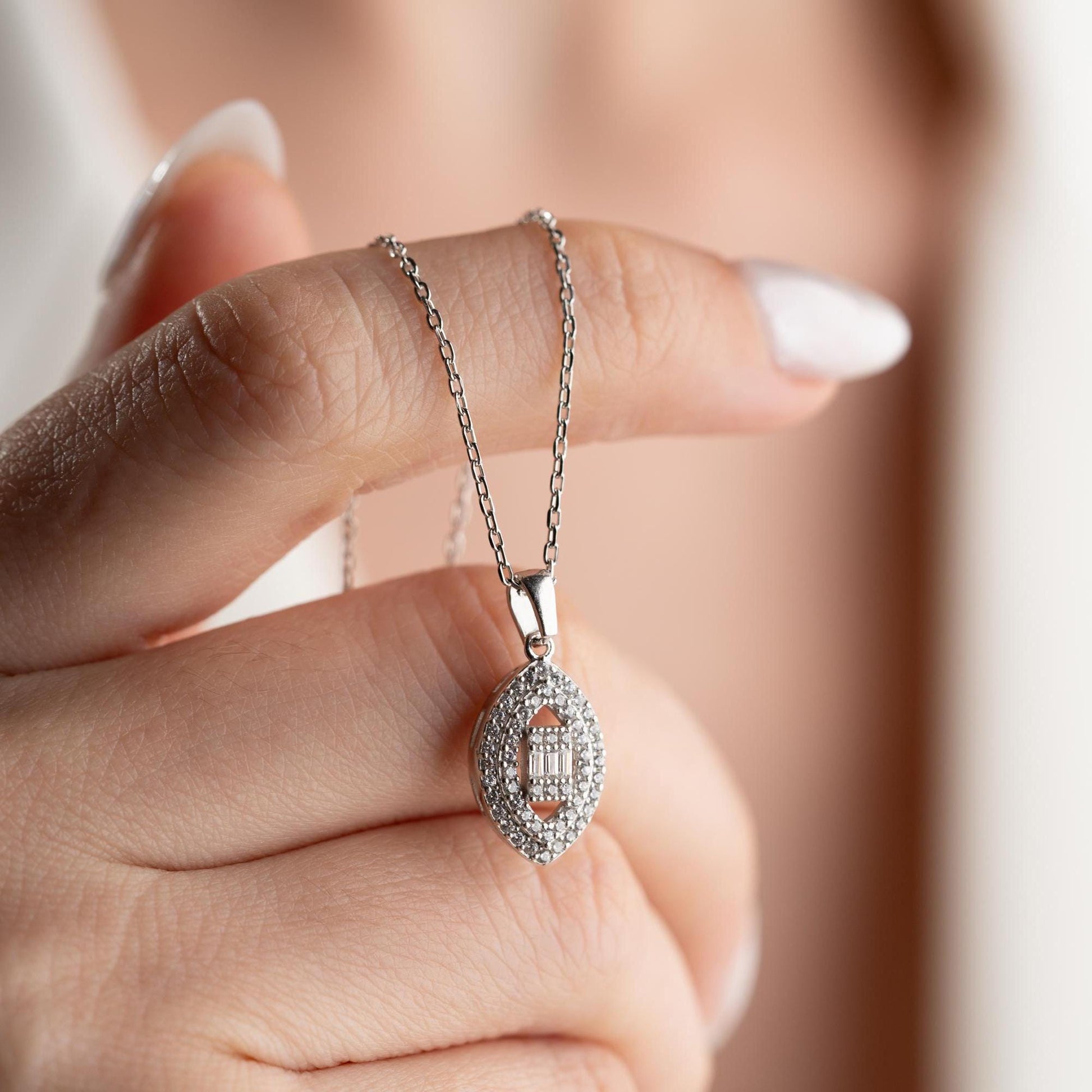 Elegant oval pendant necklace with cubic zirconia stones, available in 925 sterling silver and 14K gold plated options, displayed on a white satin background.