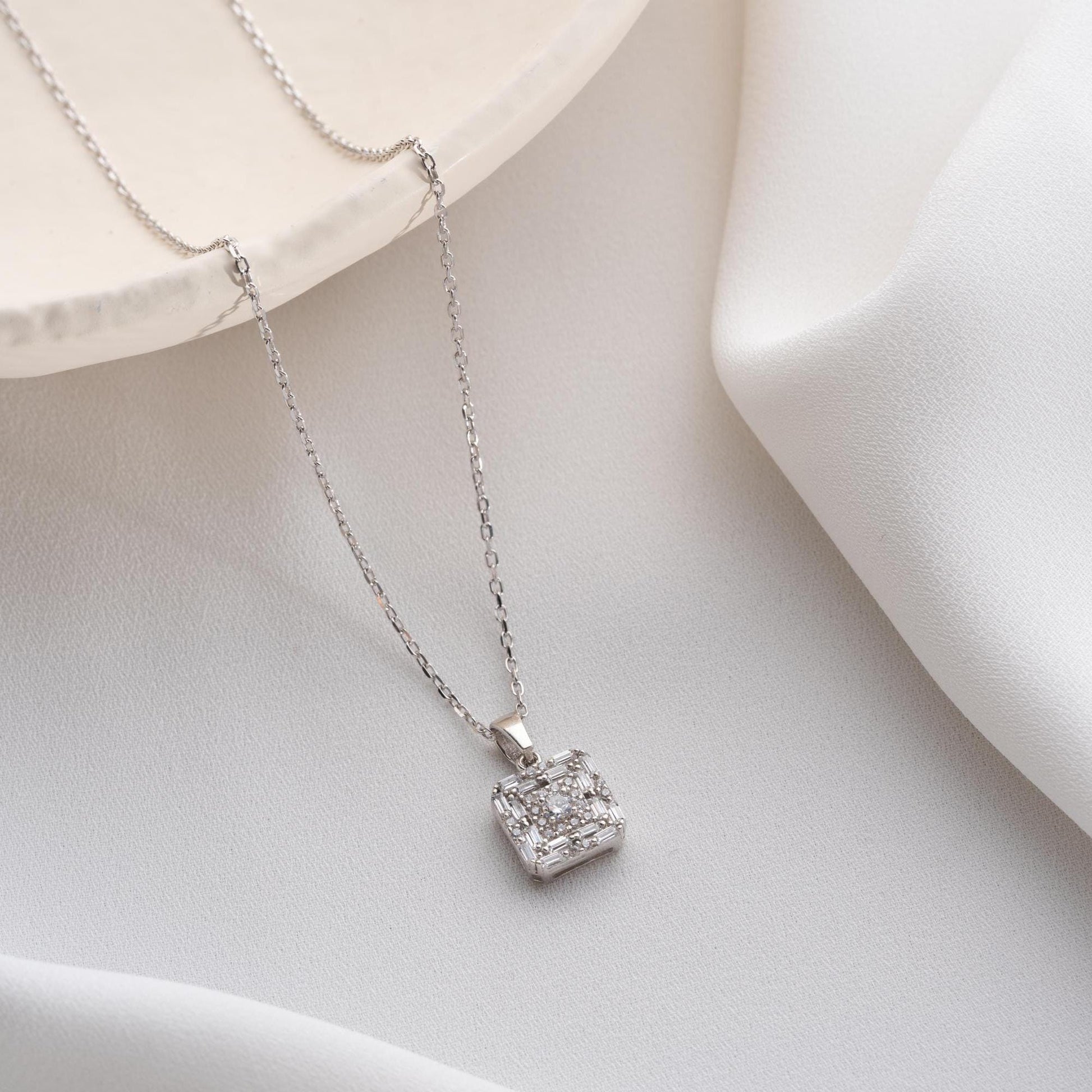 Square pendant necklace with cubic zirconia stones, available in 925 sterling silver and 14K gold plated options, displayed on a white satin background.