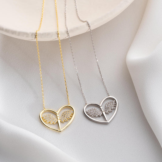 Angel wing heart necklace with cubic zirconia stones, available in 925 sterling silver and 14K gold plated options, displayed on a white satin background