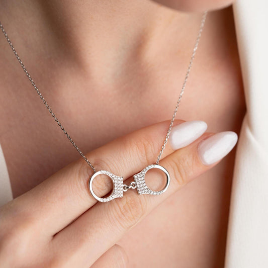 Handcuff necklace with cubic zirconia stones, available in 925 sterling silver and 14K gold plated options, displayed on a white satin background.