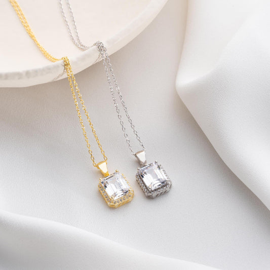 Emerald-cut pendant necklace with cubic zirconia stones, available in 925 sterling silver and 14K gold plated options, displayed on a white satin background.