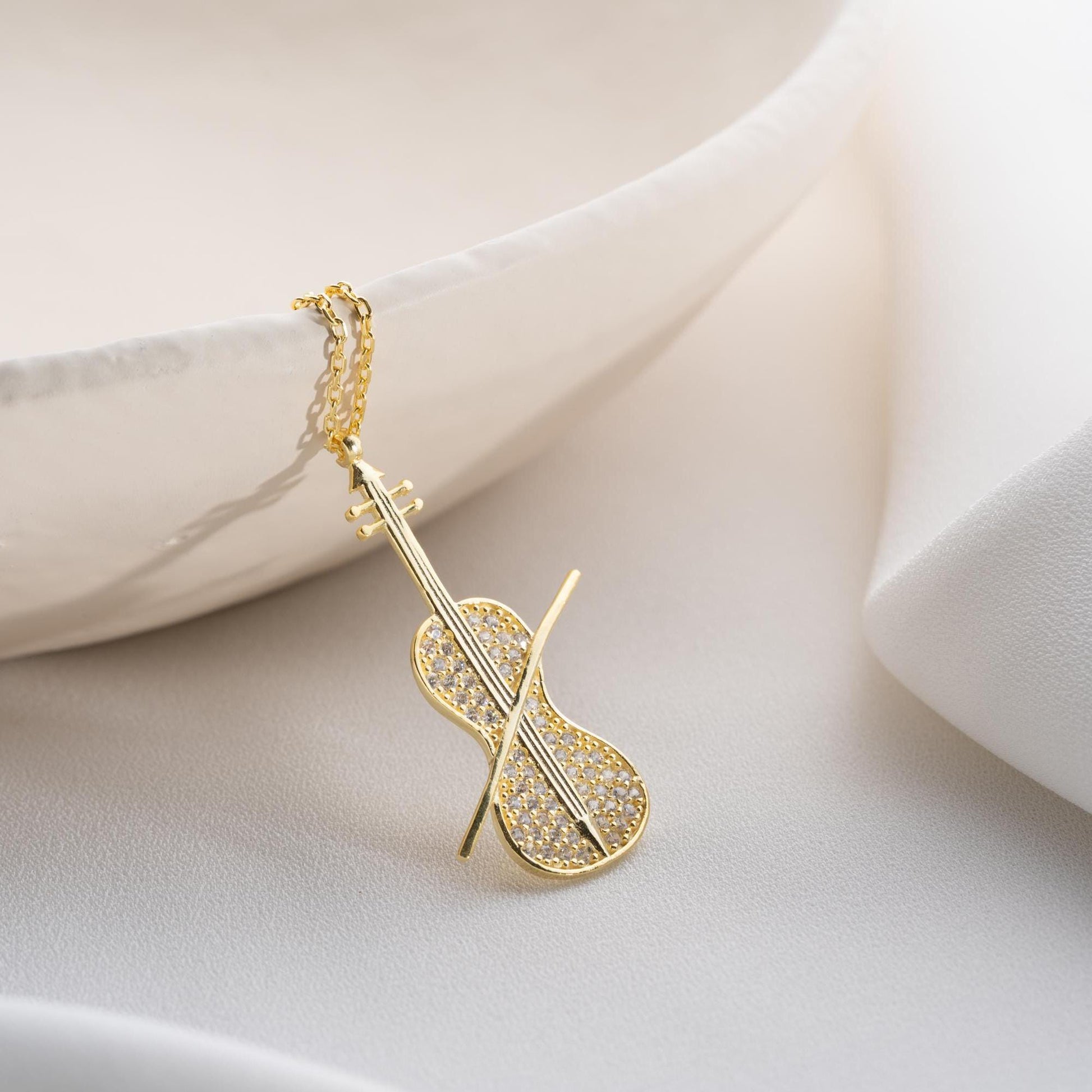 Violin-shaped necklace with cubic zirconia stones, available in 925 sterling silver and 14K gold plated options, displayed on a white satin background.