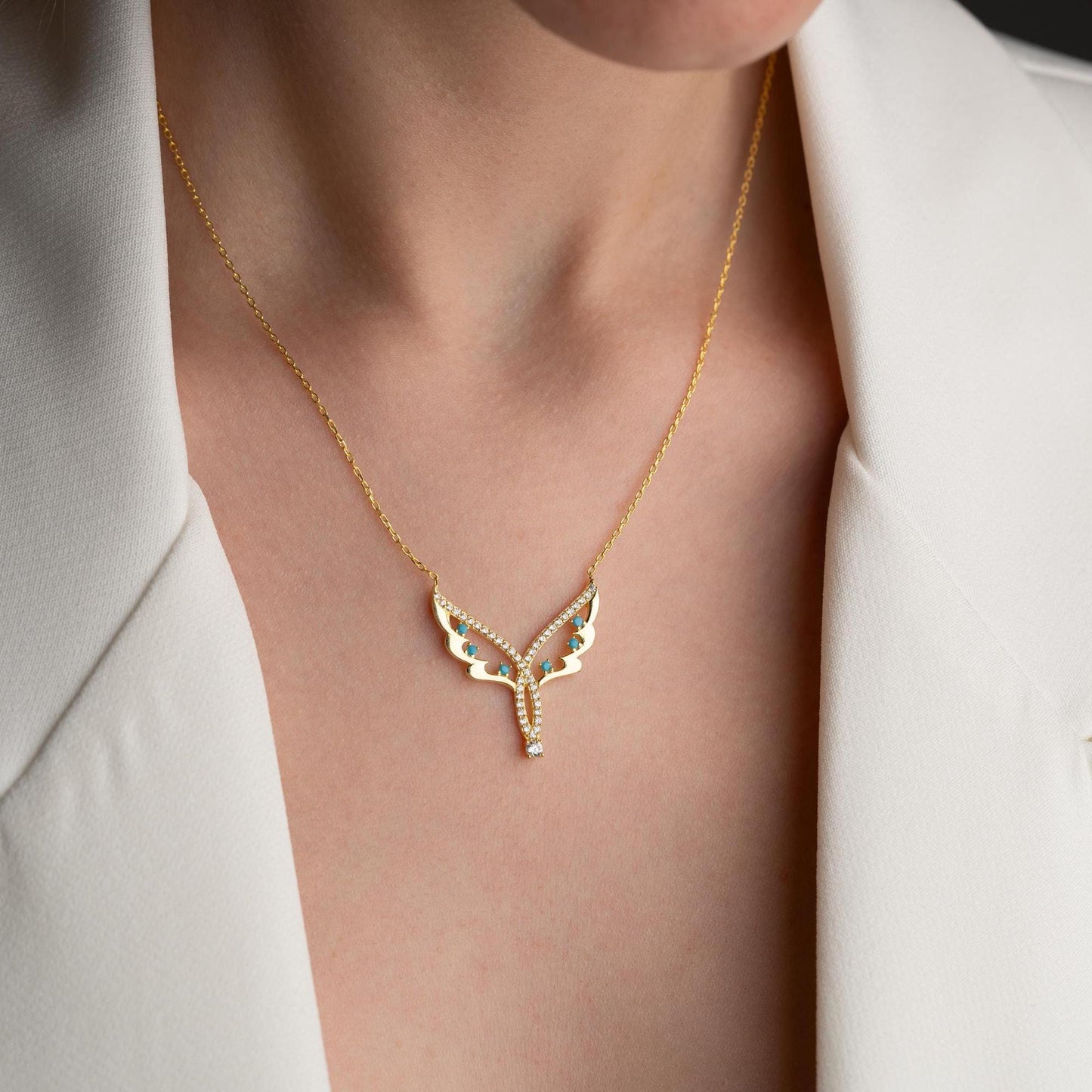 Angel wing necklace with turquoise and cubic zirconia stones, available in 925 sterling silver and 14K gold plated options, displayed on a white satin background