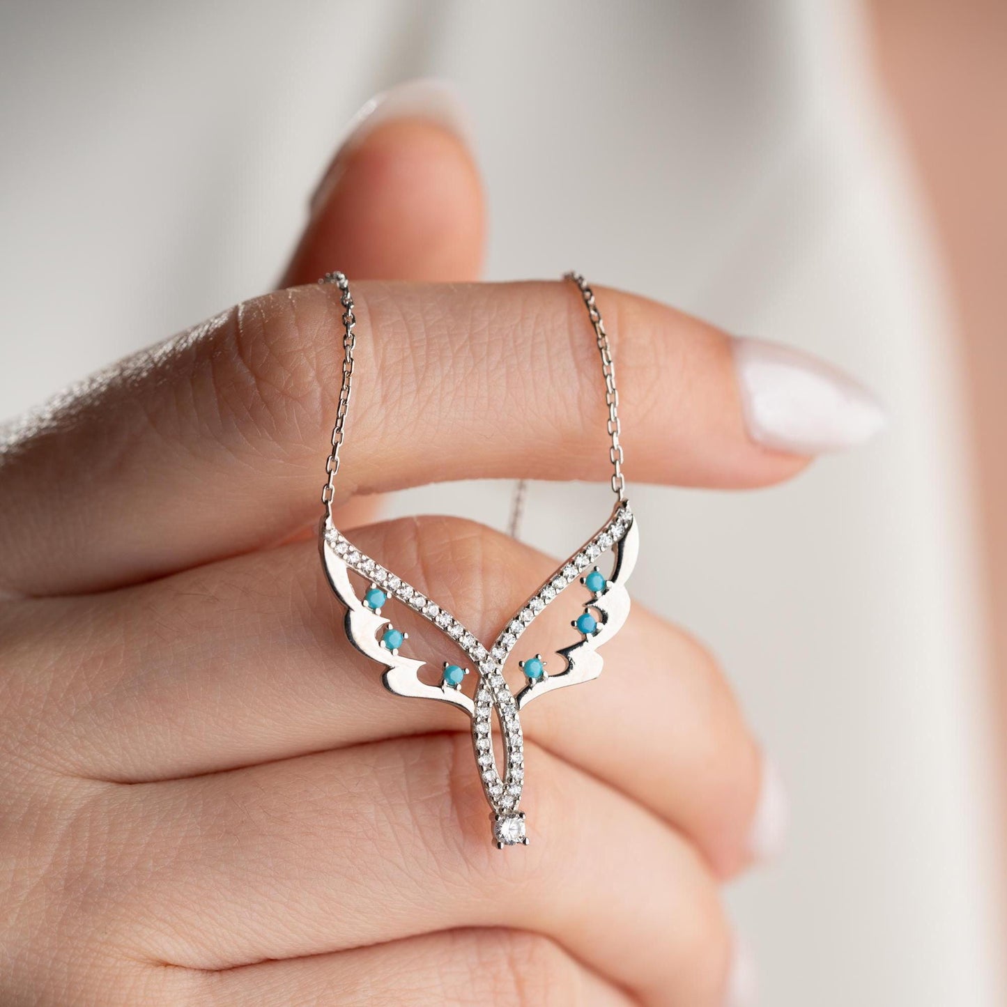 Angel wing necklace with turquoise and cubic zirconia stones, available in 925 sterling silver and 14K gold plated options, displayed on a white satin background