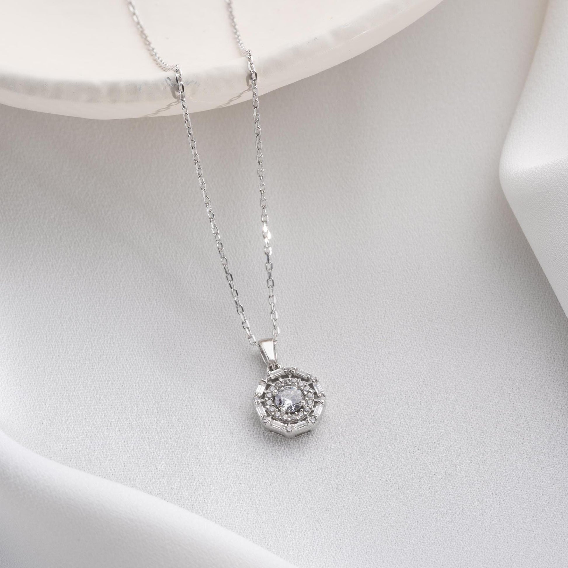 Halo pendant necklace with cubic zirconia stones, available in 925 sterling silver and 14K gold plated options, displayed on a white satin background.