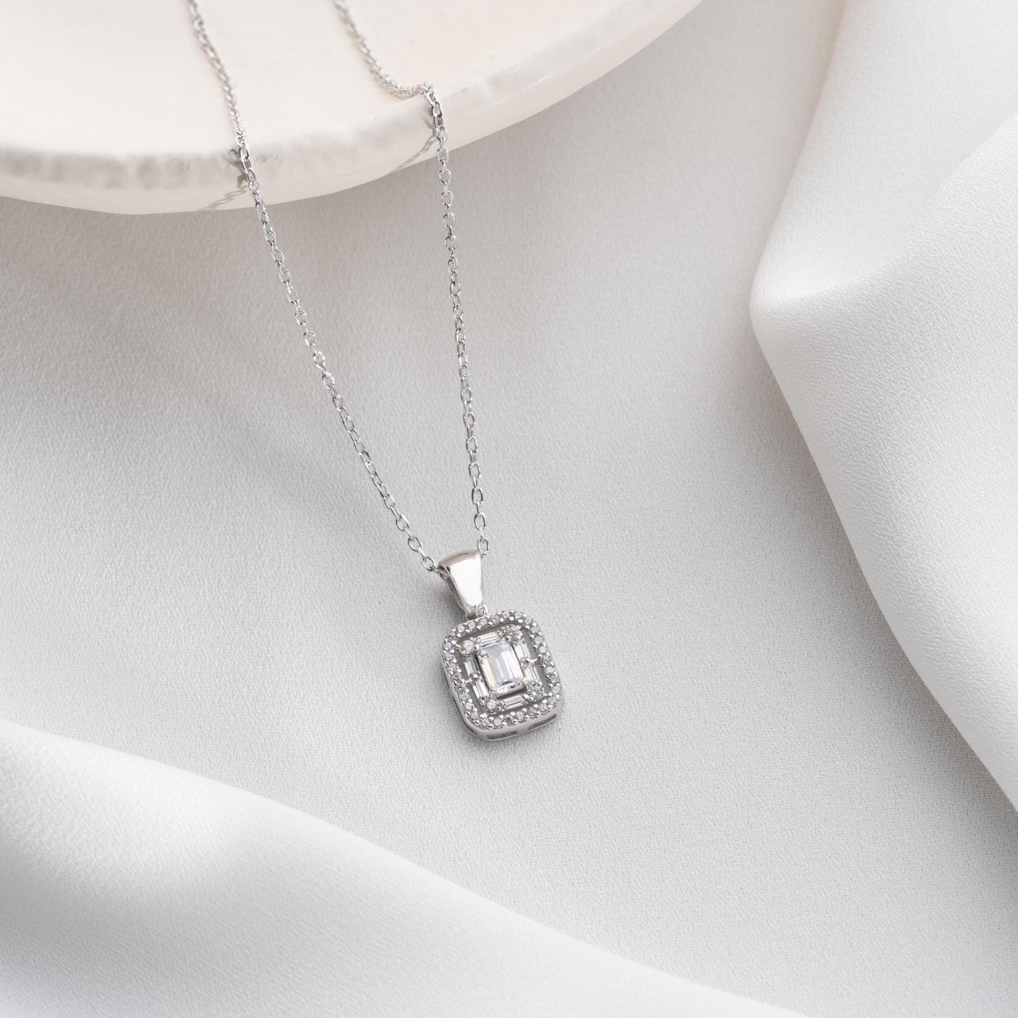Square baguette pendant necklace with cubic zirconia stones, available in 925 sterling silver and 14K gold plated options, displayed on a white satin background.