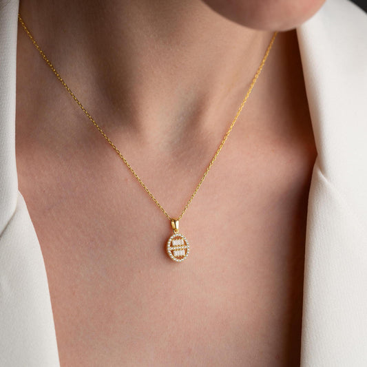 Oval pendant necklace with cubic zirconia stones, available in 925 sterling silver and 14K gold plated options, displayed on a white satin background