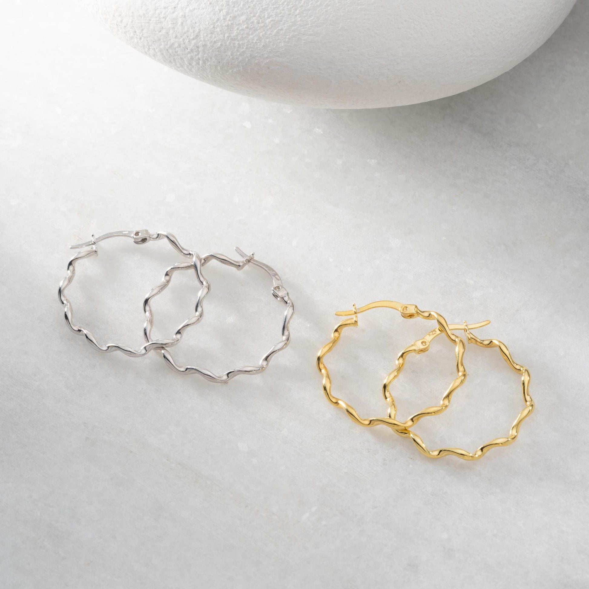 Wavy hoop earrings in 925 sterling silver and 14K gold plated options, displayed on a marble background