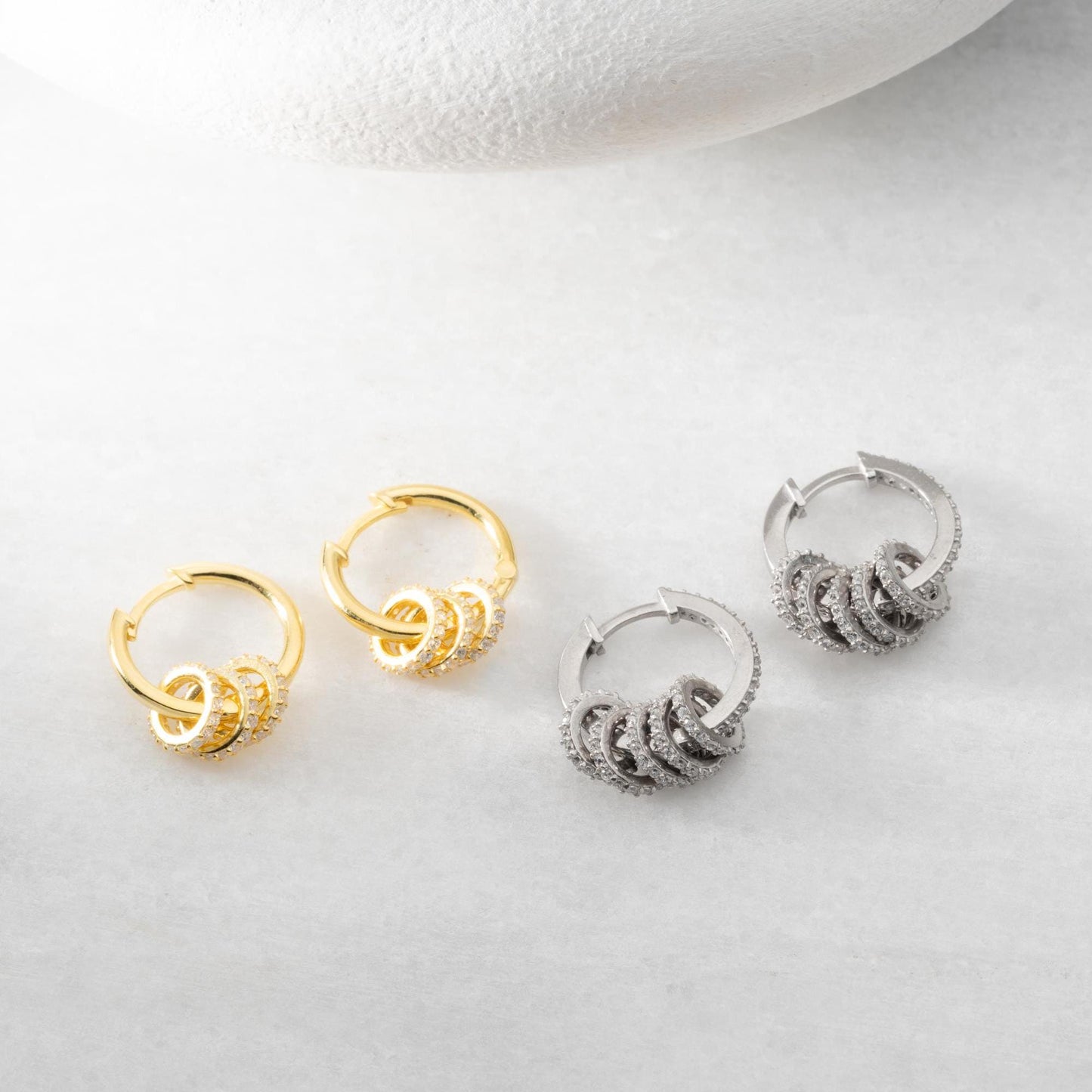 Multi-ring hoop earrings with sparkling cubic zirconia stones in 925 sterling silver and 14K gold-plated options, displayed on a marble background.