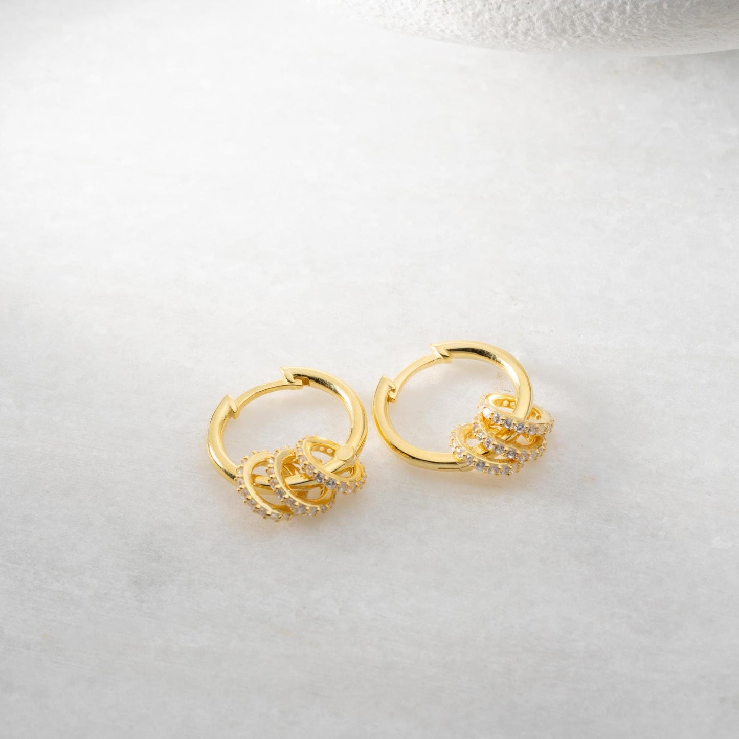 Multi-ring hoop earrings with sparkling cubic zirconia stones in 925 sterling silver and 14K gold-plated options, displayed on a marble background.