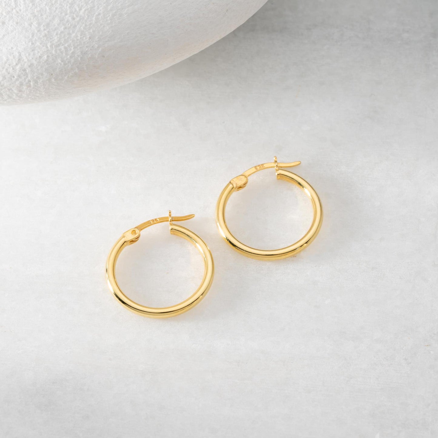 classic hoop earrings in 925 sterling silver and 14K gold plated options, featuring a minimalist polished design displayed on a marble background