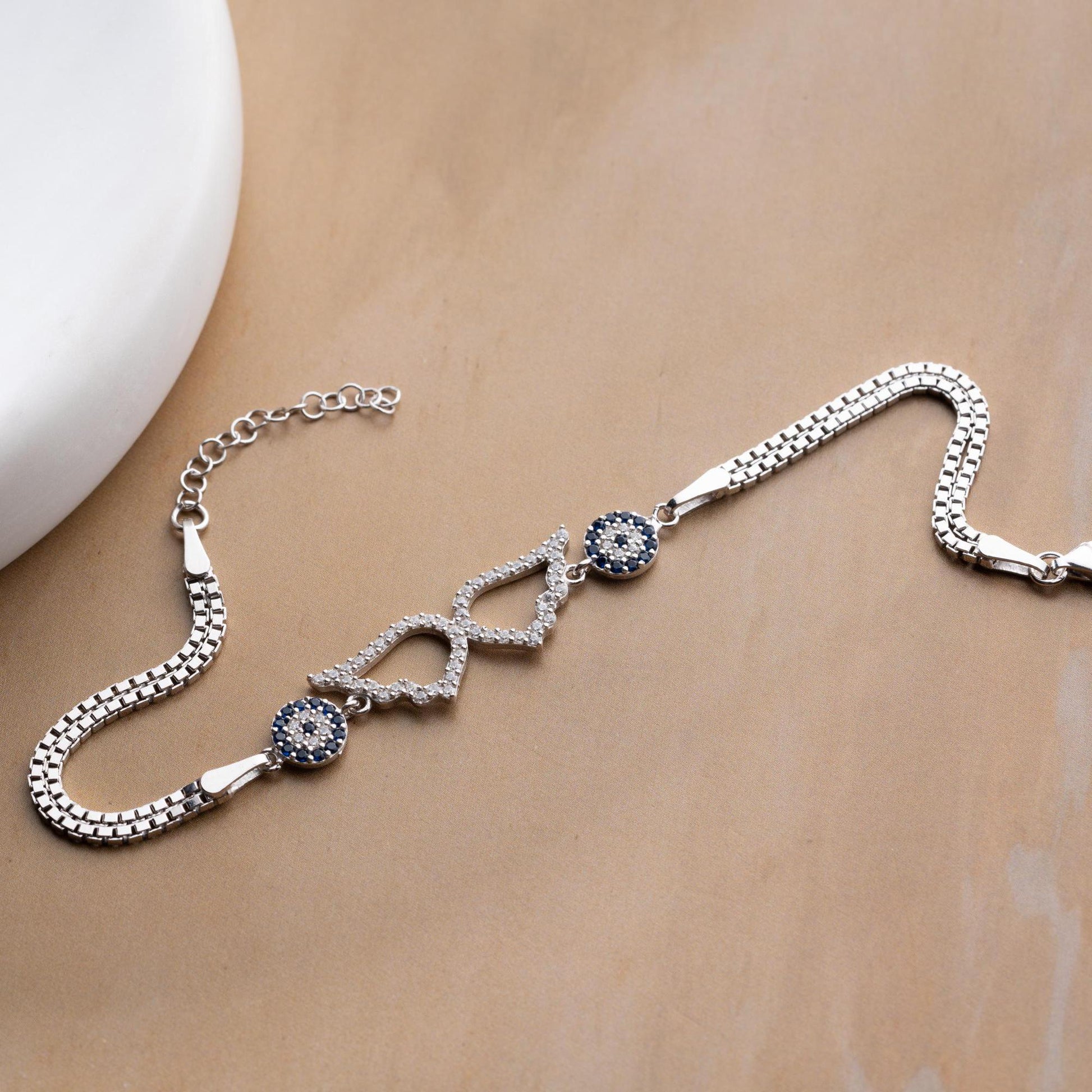 A luxurious Turkish-inspired evil eye and angel wing charm bracelet crafted in 925 sterling silver with sparkling cubic zirconia stones, available in gold and silver options.