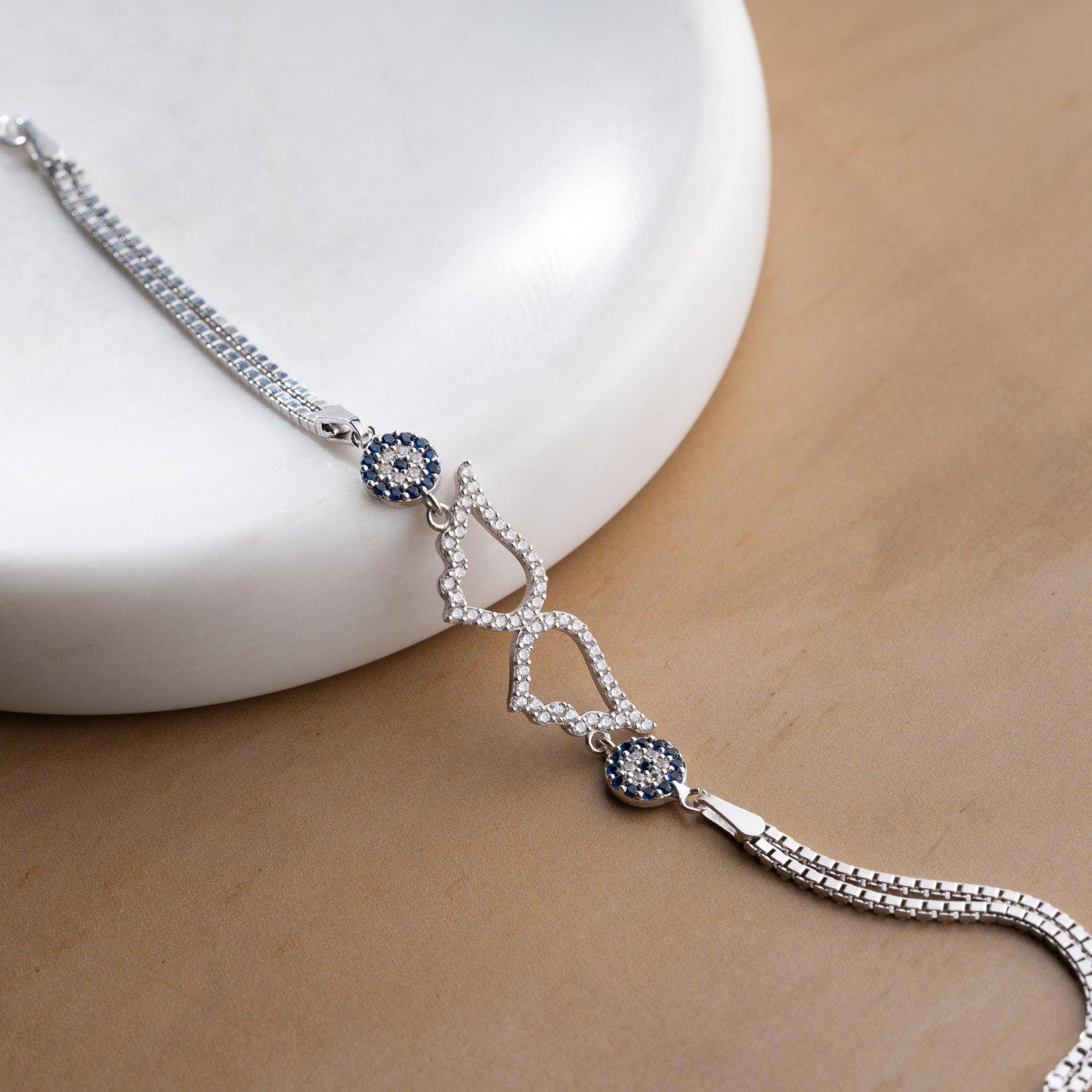 A luxurious Turkish-inspired evil eye and angel wing charm bracelet crafted in 925 sterling silver with sparkling cubic zirconia stones, available in gold and silver options.
