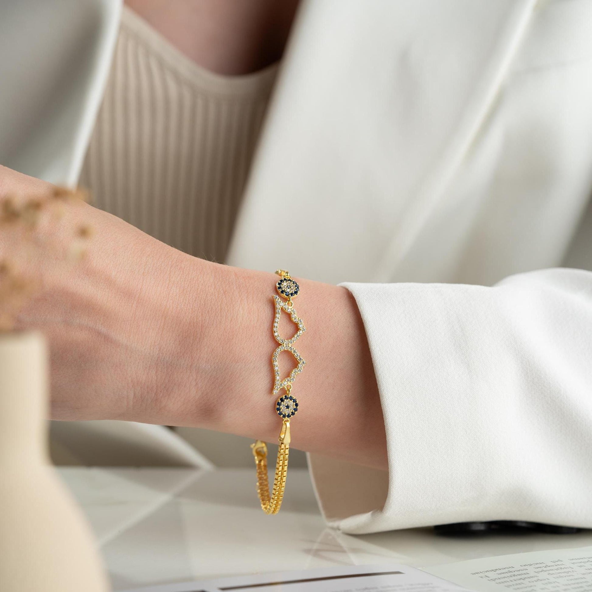 A luxurious Turkish-inspired evil eye and angel wing charm bracelet crafted in 925 sterling silver with sparkling cubic zirconia stones, available in gold and silver options.