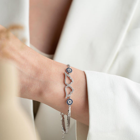 A luxurious Turkish-inspired evil eye and angel wing charm bracelet crafted in 925 sterling silver with sparkling cubic zirconia stones, available in gold and silver options.