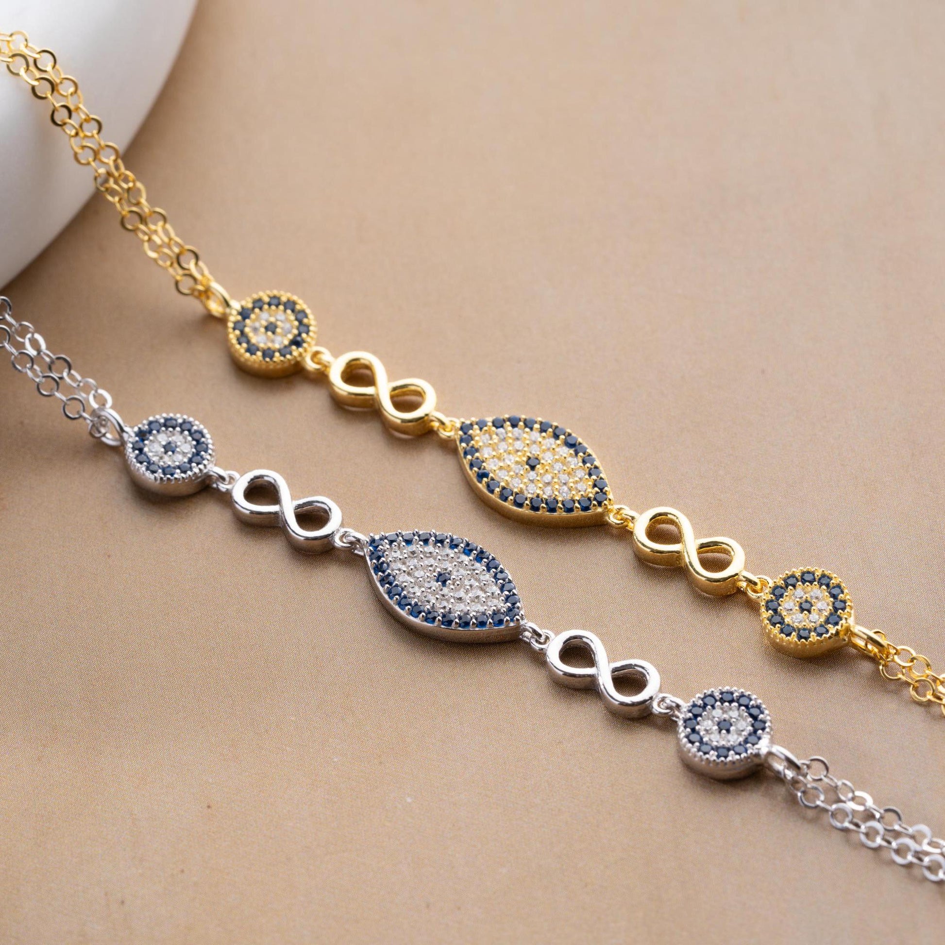 Elegant charm bracelet featuring evil eye and infinity symbols, crafted in 925 Sterling Silver with cubic zirconia stones, available in silver and gold finishes.