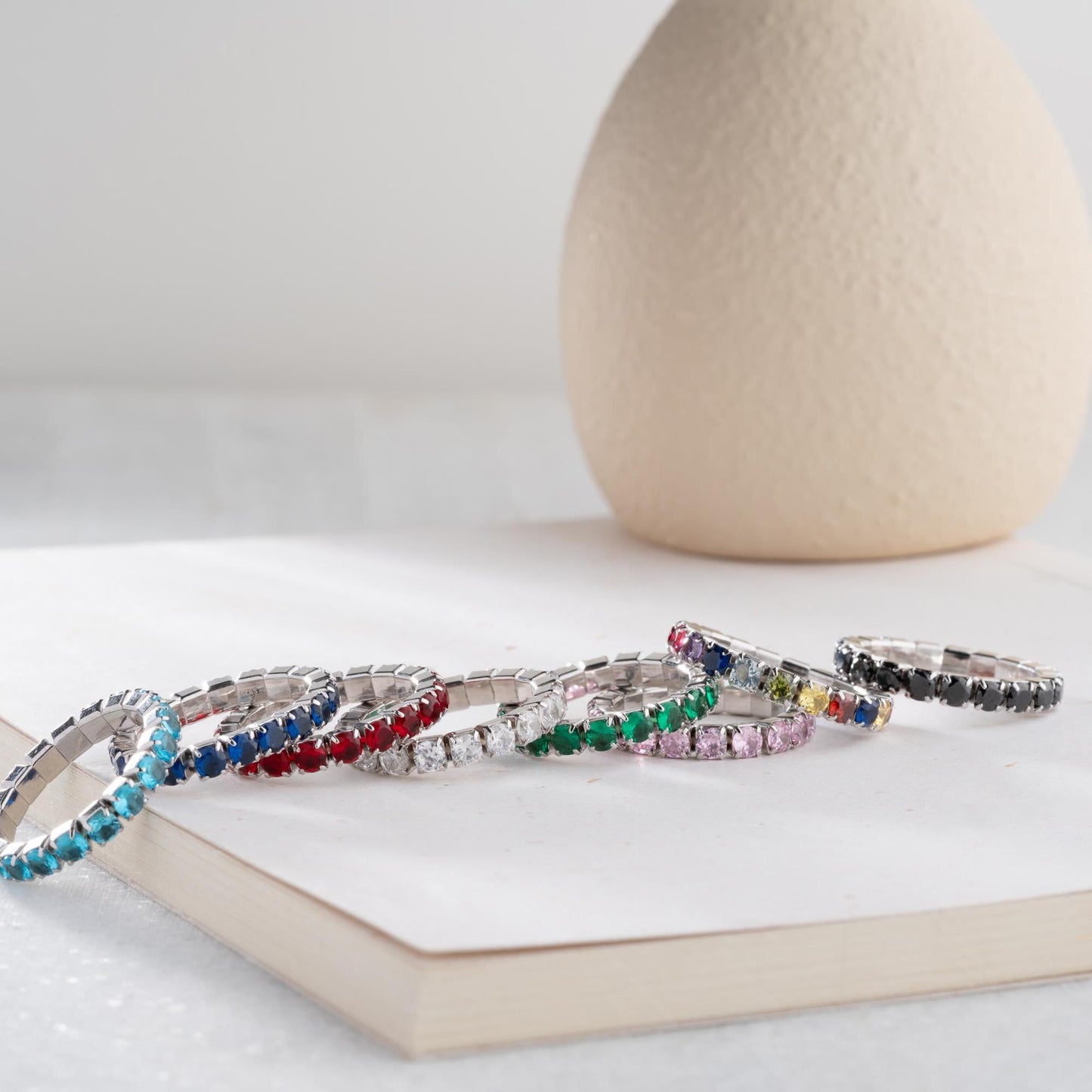 Single vibrant tennis ring crafted in 925 Sterling Silver with colorful cubic zirconia stones, available in rainbow, red, blue, green, black, and pink.